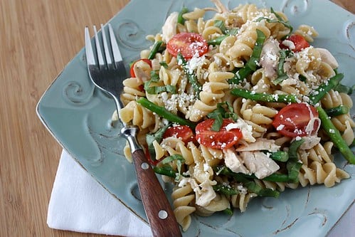 Basil chicken pasta salad on a blue plate with a wood handled fork.