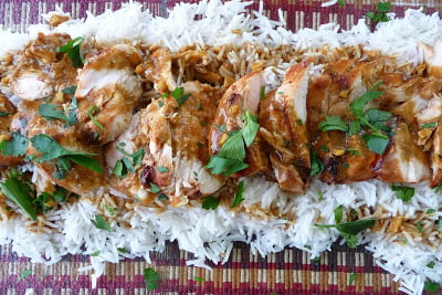 Sliced grilled chicken, rice and sauce on a platter.