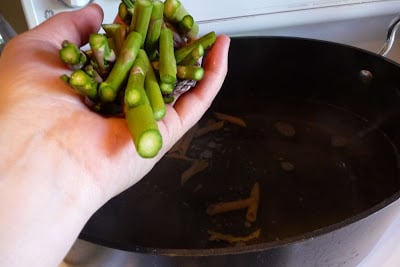 A hand holding asparagus over a pot of water.
