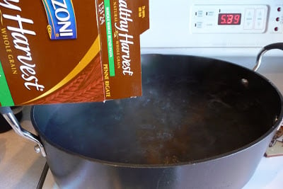 Pouring whole wheat pasta into a pot of boiling water.