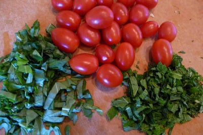 Chopped herbs and grape tomatoes on a cutting board.