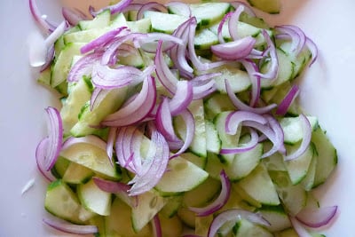 Cucumber slices and red onion slices in a white bowl.