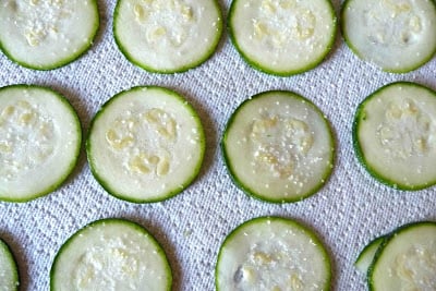 Salted slices of zucchini on a paper towel.