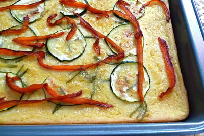 Chickpea focaccia (farinata) topped with zucchini and peppers in a pan.