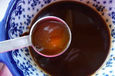 A teaspoon filled with sesame oil over a bowl of soy sauce.