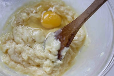 Egg, dough and wooden spoon in a glass bowl.