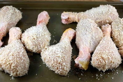 Breadcrumb-coated chicken drumsticks on a baking sheet.