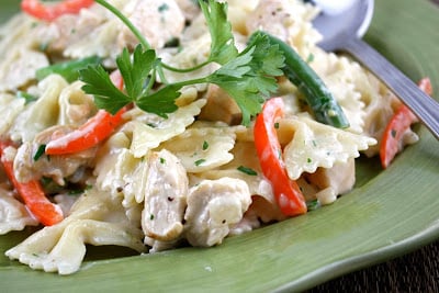 Bowtie pasta in a cream sauce, with chicken and vegetables, on a green plate.