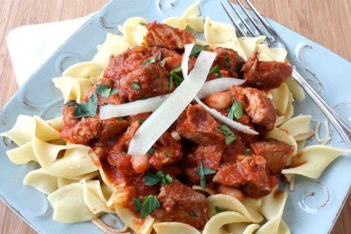 Braised country style pork ribs in tomato sauce with pasta on a blue plate.
