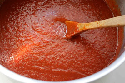 Tomato sauce and wooden spoon in a large saucepan.