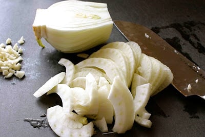Slices of raw fennel and a chef's knife on a cutting board.
