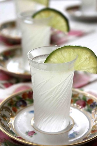 A cut glass shot glass filled with liquid, lime on the side.