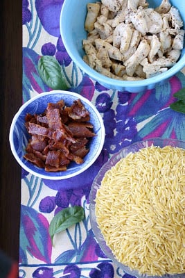 Bowls of cooked bacon, chicken and orzo pasta on a colorful tablecloth.