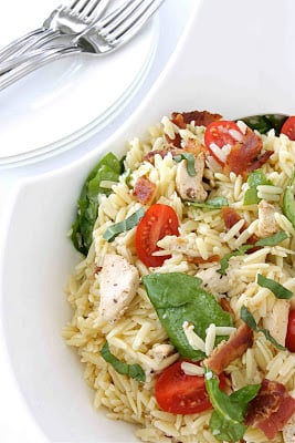 White bowl filled with orzo pasta salad with tomatoes, bacon and spinach.