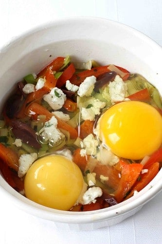 Raw eggs, vegetables and cheese in a ramekin.