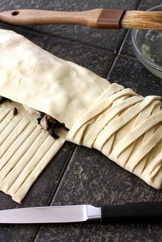 A rolled puff pastry strudel, halfway through decorating with strips of puff pastry.