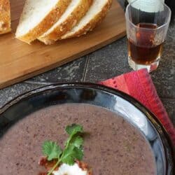 Black bean soup in a black bowl, with sliced bread on the side.