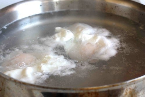An egg poaching in a pan of simmering water.