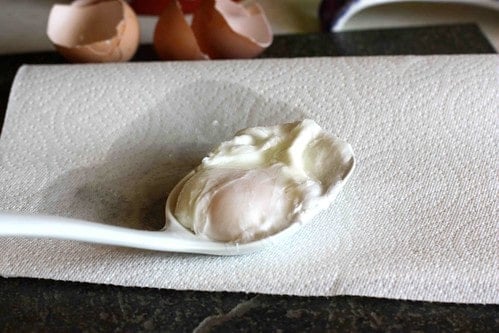 A poached egg in a spoon, resting on a paper towel.