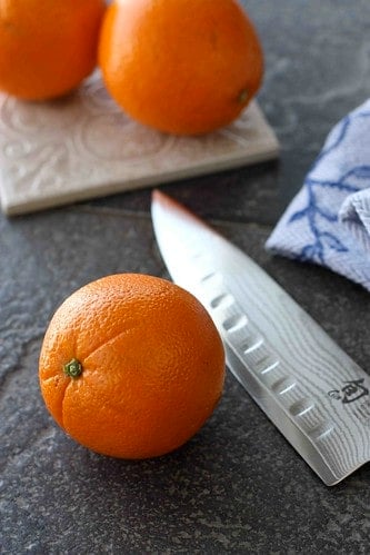 Navel oranges and a chef's knife on a black surface.