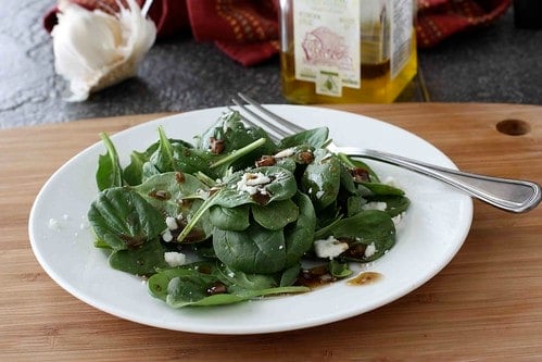 A spinach salad on a white plate, topped with balsamic vinaigrette.