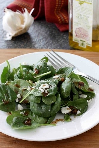 A spinach salad on a white plate, topped with balsamic vinaigrette.