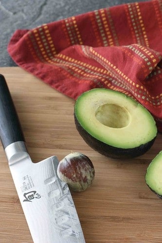 Halved avocado and chef's knife on a cutting board.