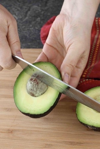An avocado half with the base of a knife in the pit.
