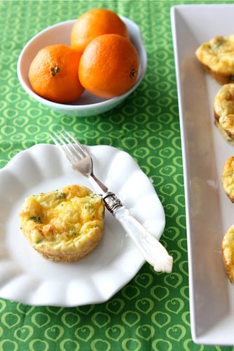 Mini egg muffins on a white plate. A bowl of oranges behind.