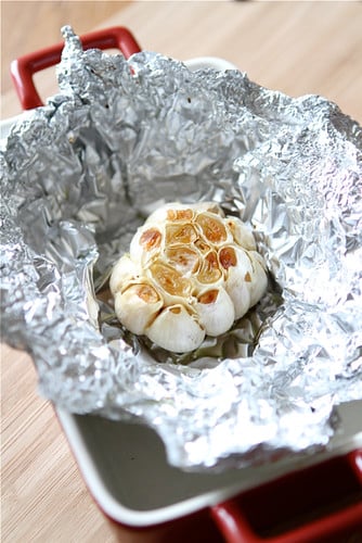 Roasted bulb of garlic on foil inside a small casserole dish.