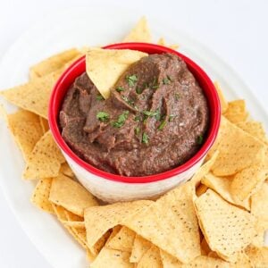 Black bean dip in a red bowl, on a white plate with tortilla chips.