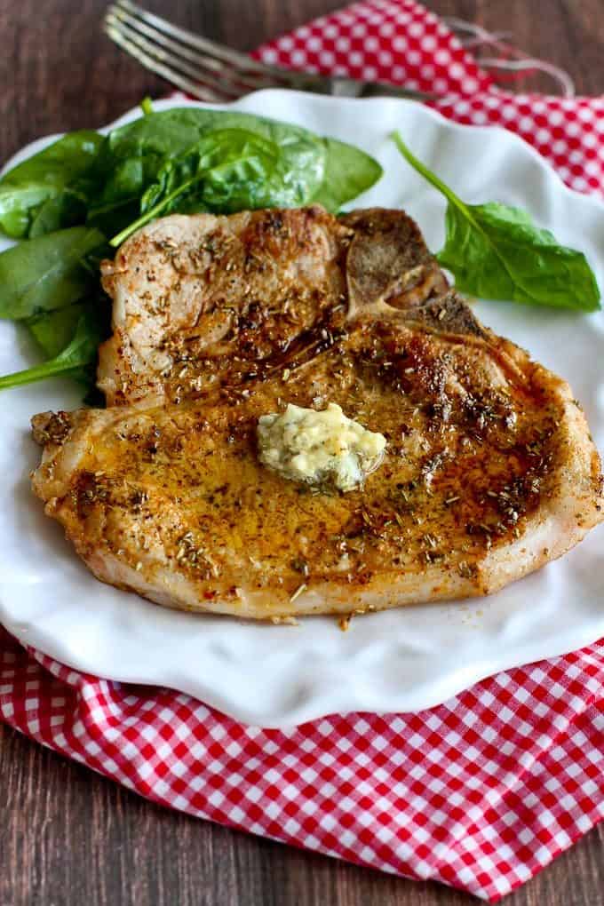 Garlic butter pork chops on a white plate with spinach leaves.