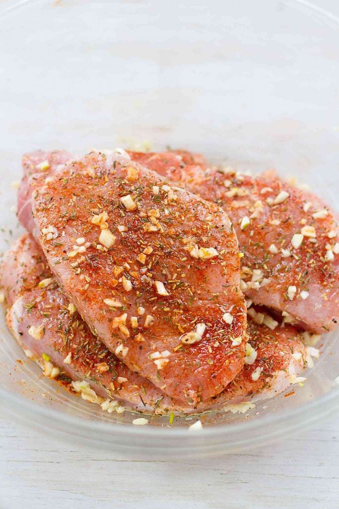 Raw porks chops, coated with spices, in a glass bowl.