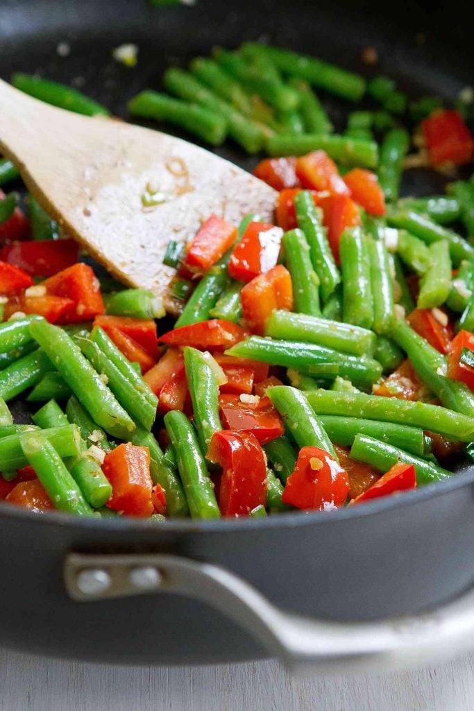 Green beans and red bell peppers being stir fried in a nonstick pan with garlic and ginger.