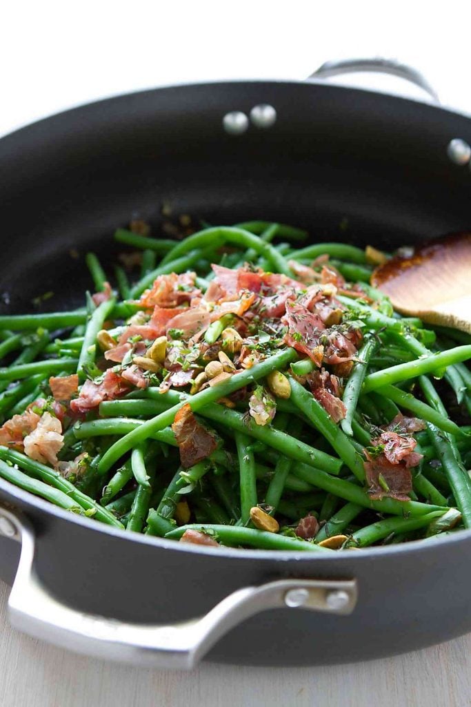 Green beans in a skillet with crisp prosciutto, toasted pistachios and fresh herbs.
