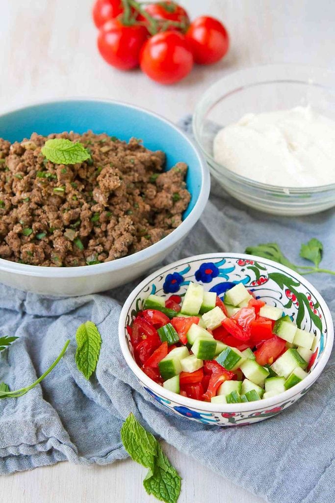 Beef kofta dip ingredients in separate bowls. Spiced ground beef, tomatoes and cucumber, and hummus with yogurt.