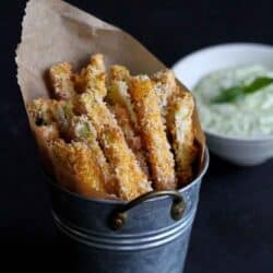 Baked zucchini fries in a metal container, yogurt dip in the background.
