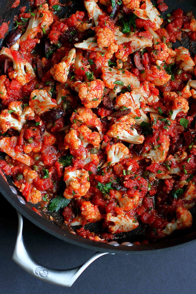 Cooked cauliflower and tomato sauce with olives in a skillet.
