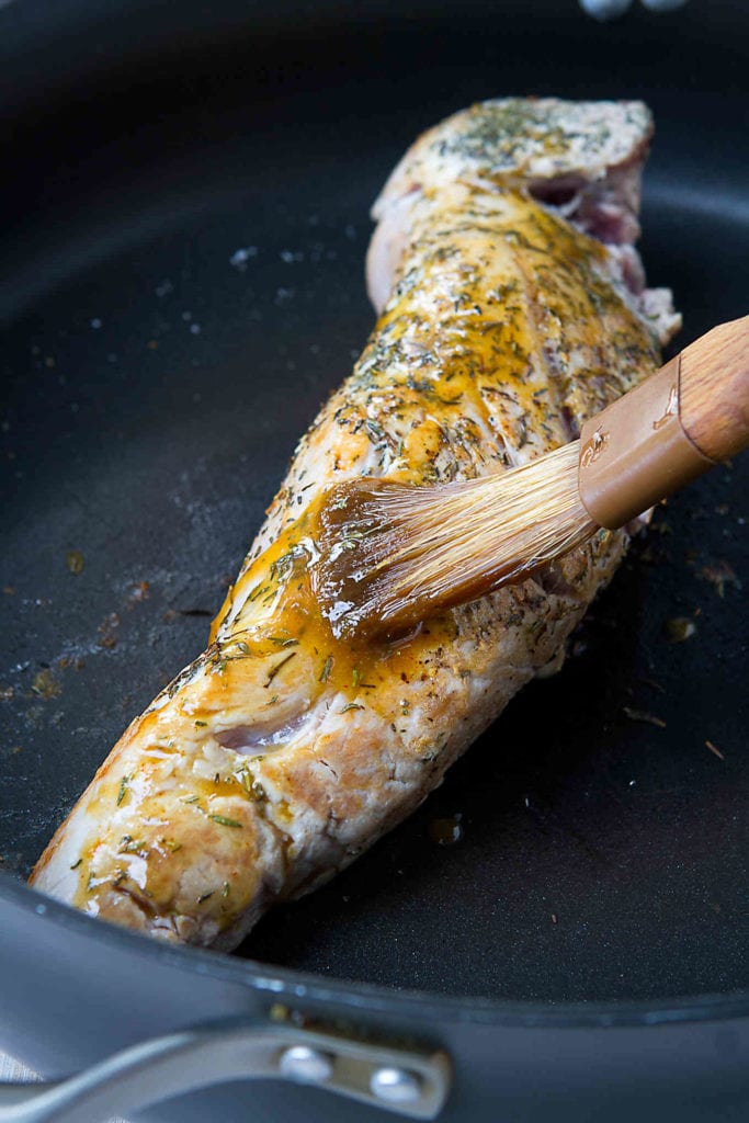 Brushing seared pork tenderloin with a maple Dijon sauce, in a nonstick skillet.