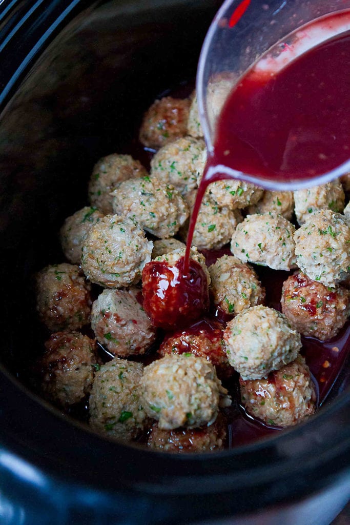Turkey meatballs in a crockpot, with blackberry chili sauce being poured over top.