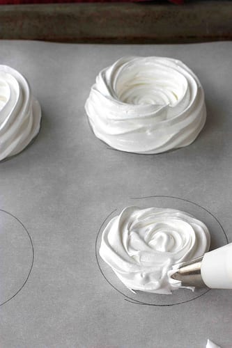 Piping meringue shells onto parchment paper.