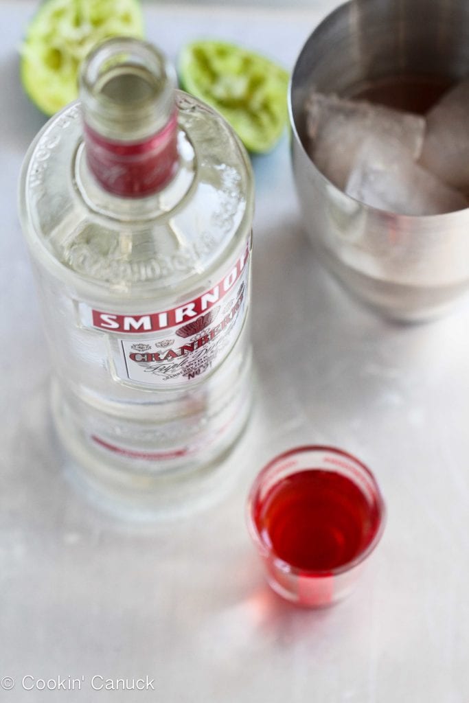Vodka, cranberry juice, lime halves and a cocktail shaker.