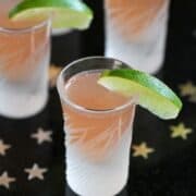 Cut glass shot glasses filled with pink cranberry infused vodka, with lime wedges.