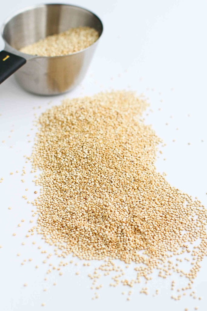 Dry quinoa and measuring cup on a white background.