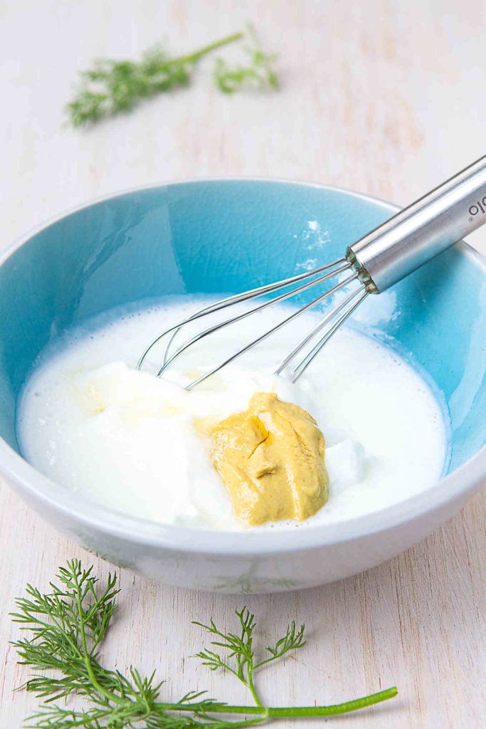 Buttermilk, yogurt and Dijon mustard in a bowl, with a whisk.