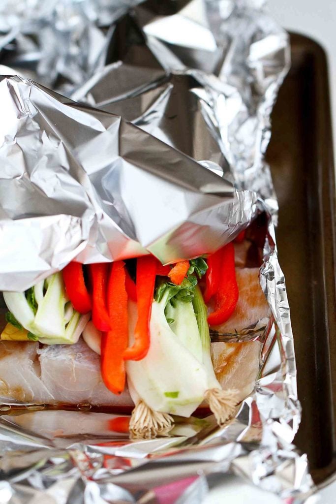 Fish fillets, with peppers and bok choy, tucked in a foil packet.