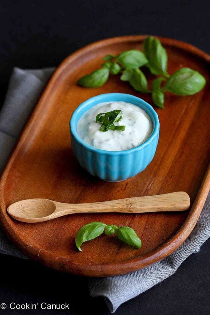 Yogurt sauce on a small wooden board, with a wooden spoon and basil leaves.