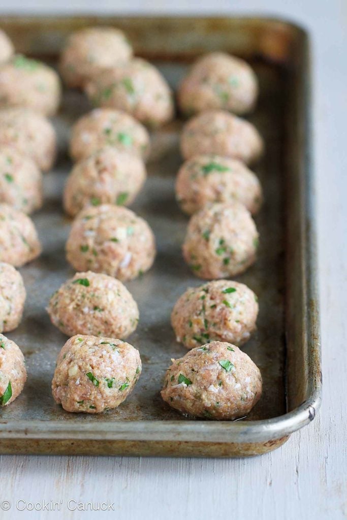 Turkey meatballs lined up on a baking sheet, ready to bake.