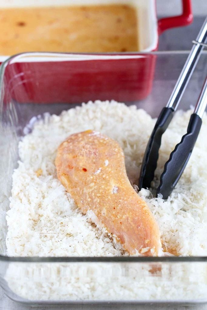 Chicken tender in panko breadcrumbs, in a glass baking dish with tongs.