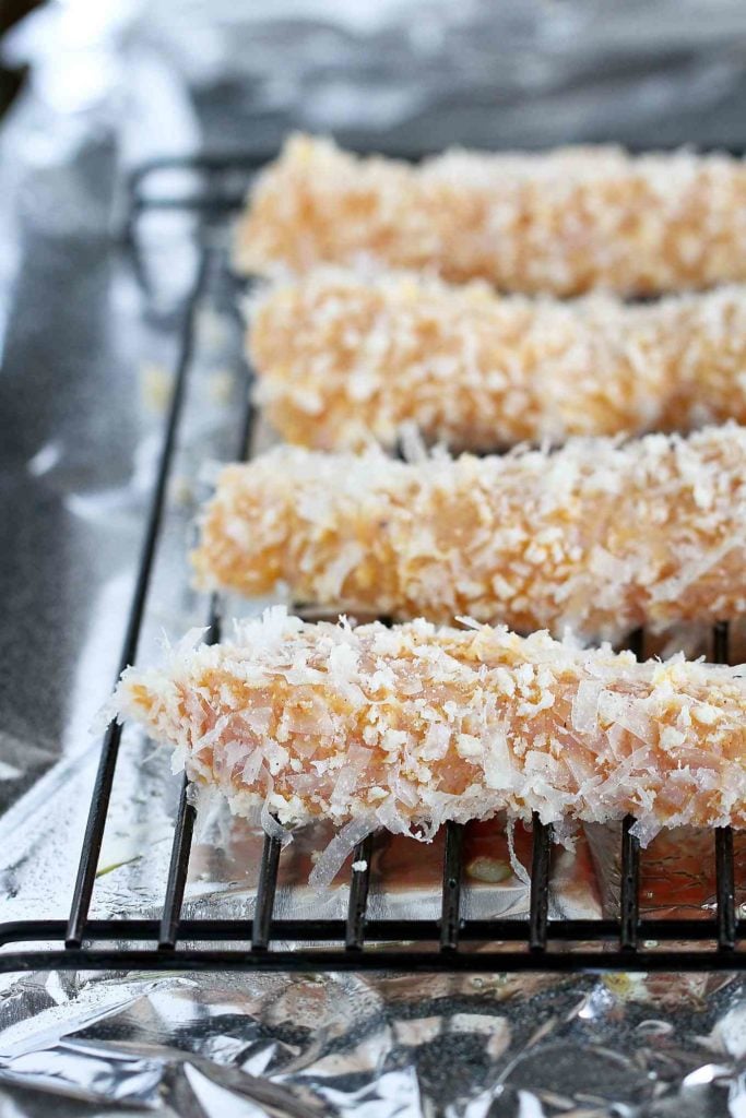 Breaded chicken tenders on a rack, set over a baking sheet that is lined with foil.